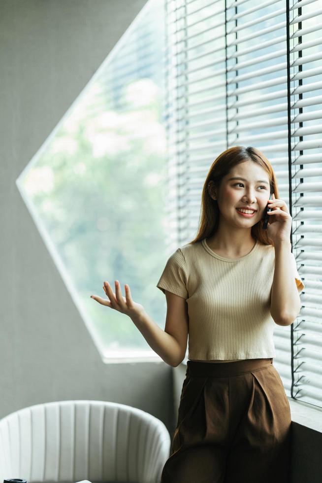 la mujer asiática con ropa informal es feliz y alegre mientras se comunica con su teléfono inteligente y trabaja en una cafetería. foto
