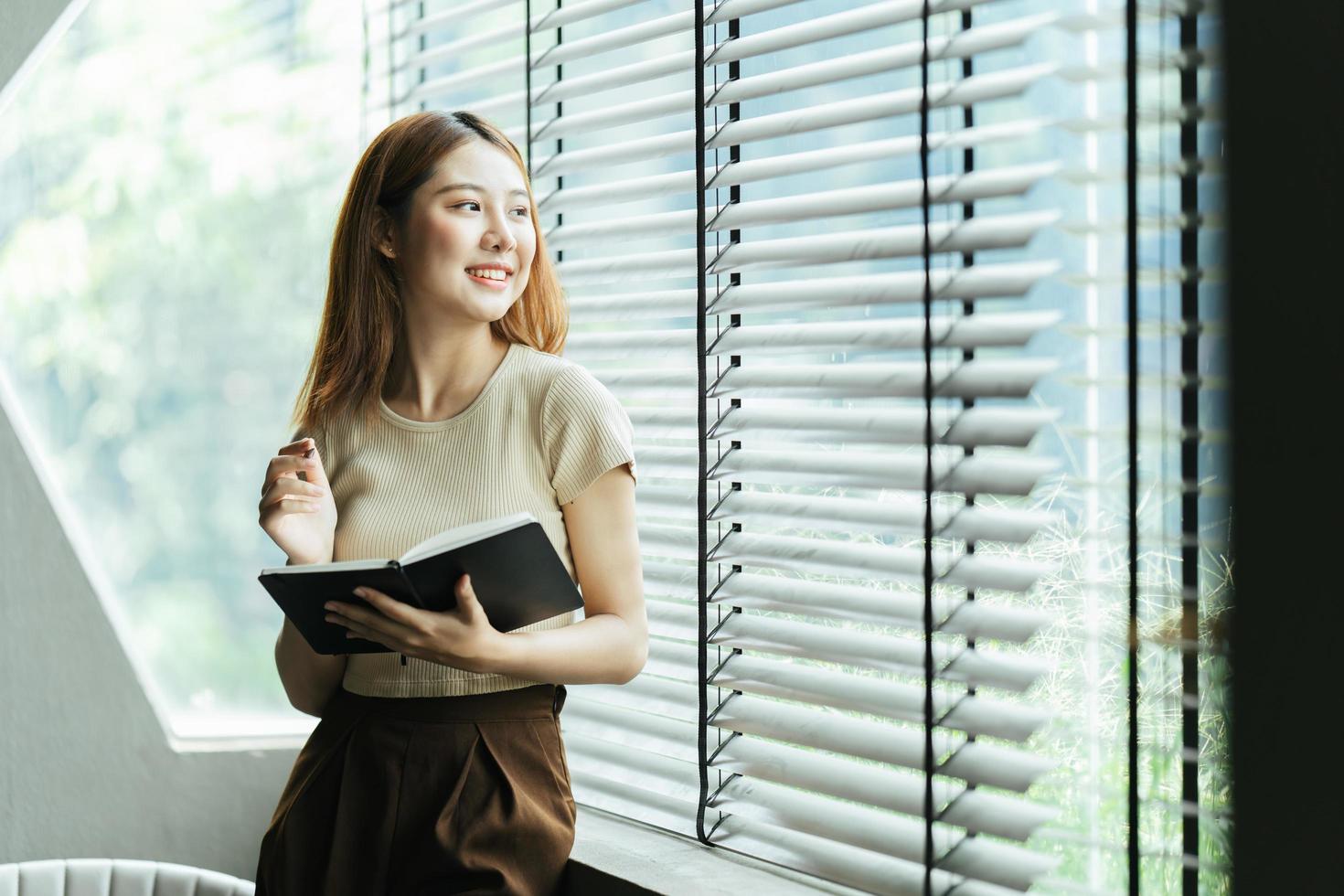 Young asian business woman is standing at a desk and taking notes in a notebook. The concept of education and technology. photo