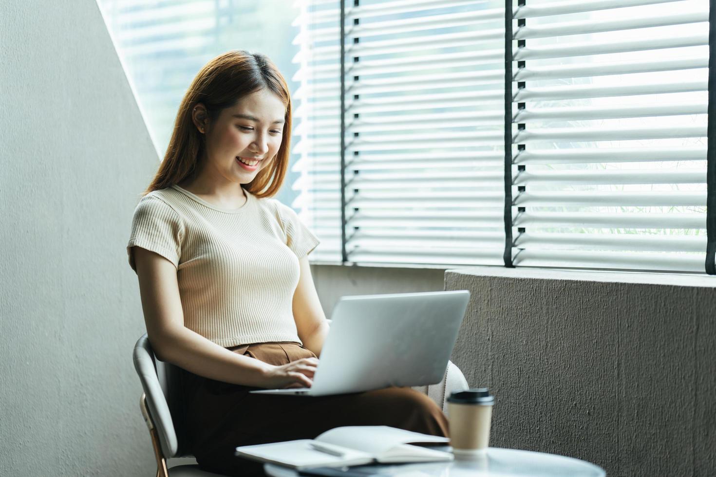 retrato de una hermosa mujer asiática sentada en el interior de un restaurante cafetería durante el verano, usando una computadora portátil y un teléfono inteligente con tecnología inalámbrica inteligente, relajándose en un café restaurante. foto