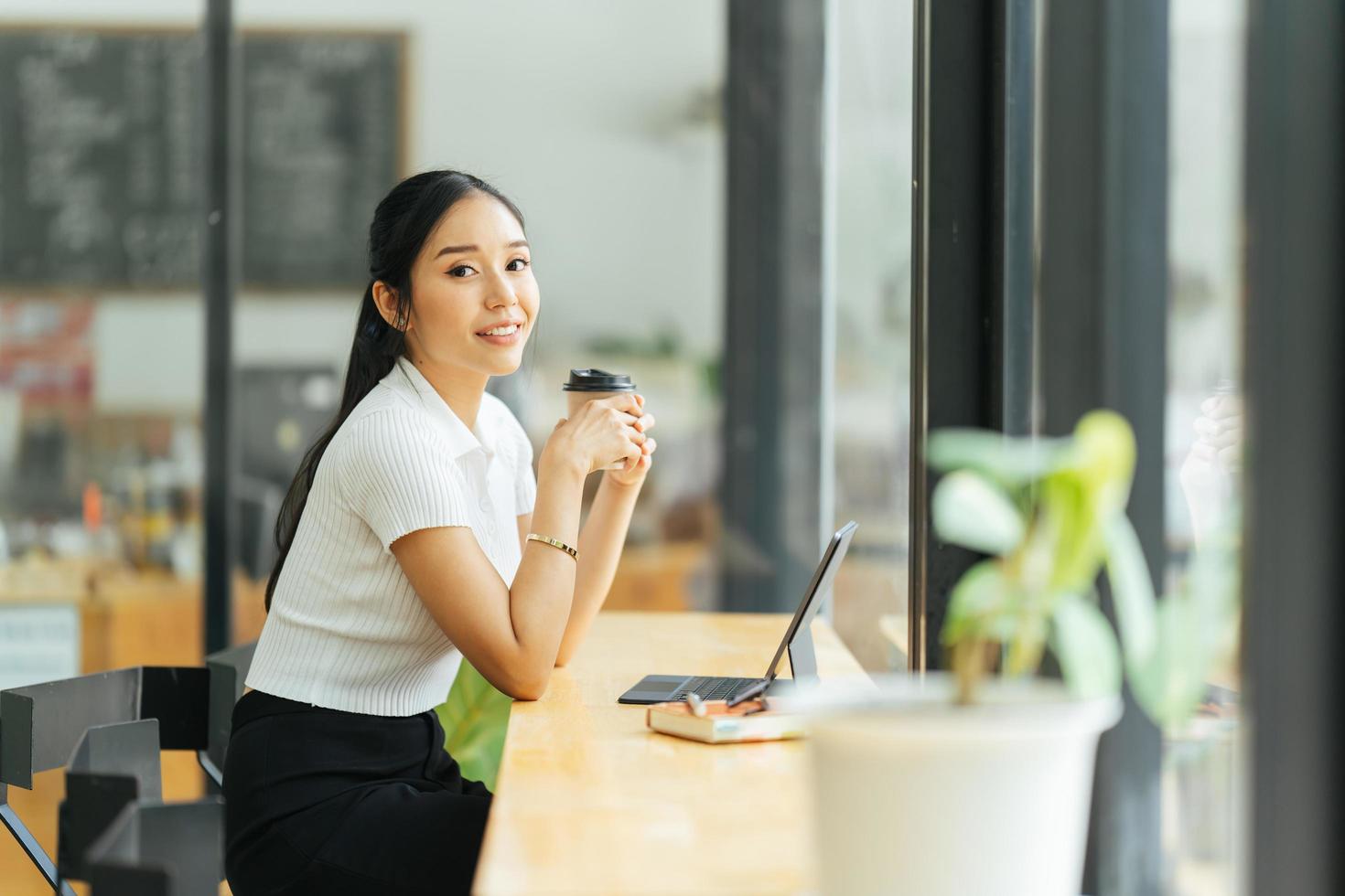 Beautiful young asian business woman drinking coffee and using laptop computer while working in office. photo