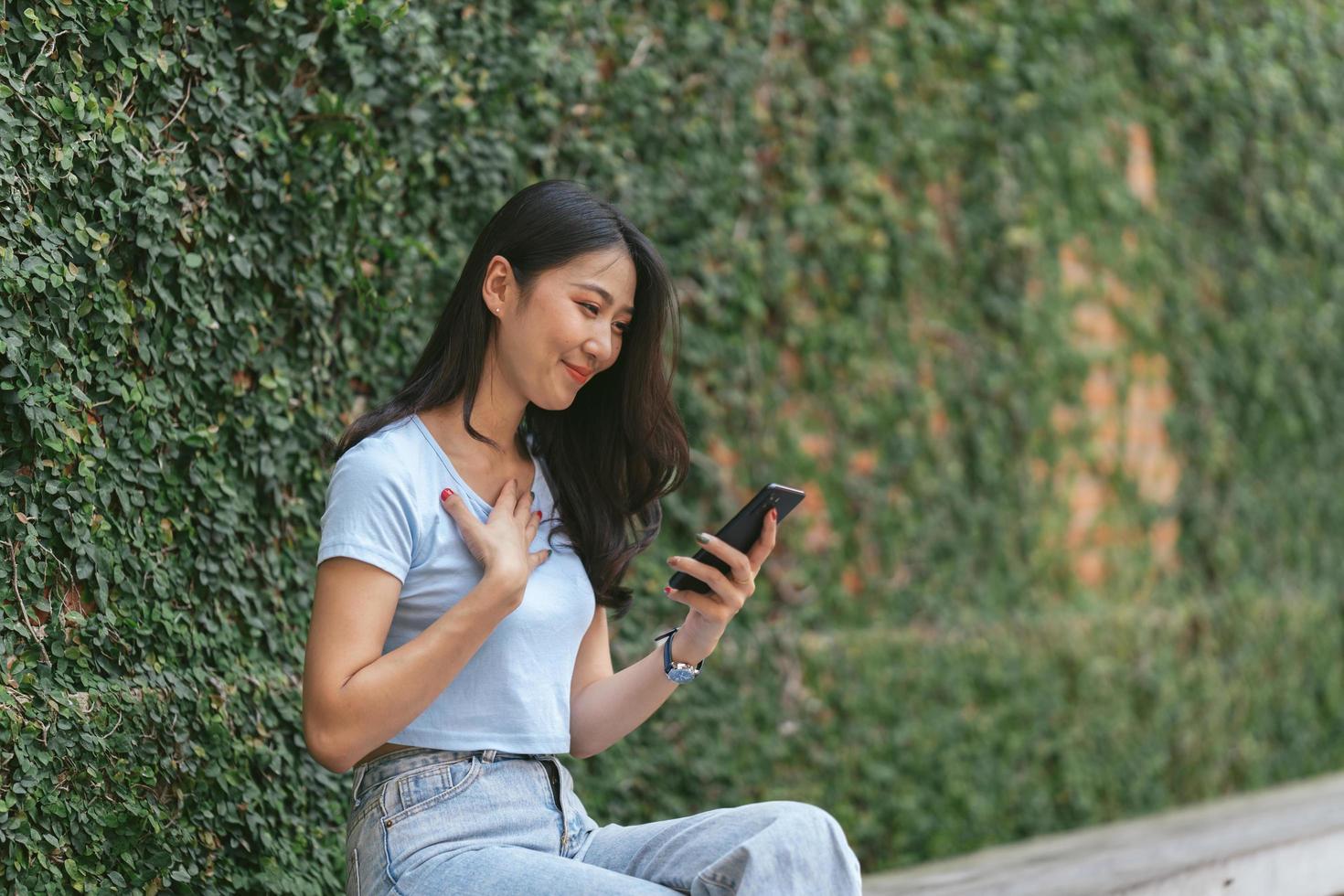 Happy asian woman smiling and holding cellphone while sitting in street summer cafe. photo