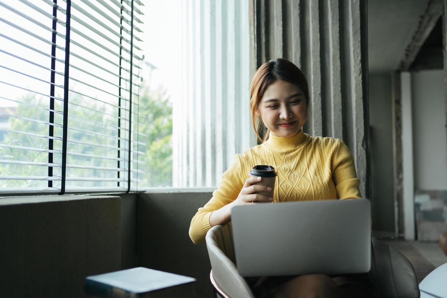 Portrait of beautiful Asian woman sitting indoors at coffee shop restaurant during summer, using smart wireless technology computer laptop and smartphone, relaxing coffee break at cafe restaurant. photo
