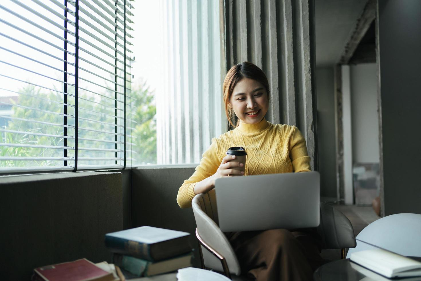 Portrait of beautiful Asian woman sitting indoors at coffee shop restaurant during summer, using smart wireless technology computer laptop and smartphone, relaxing coffee break at cafe restaurant. photo