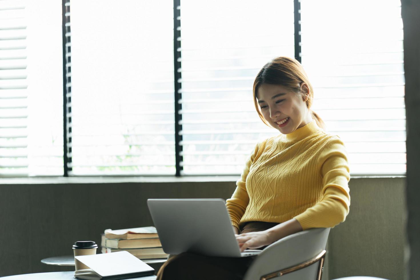 Portrait of beautiful Asian woman sitting indoors at coffee shop restaurant during summer, using smart wireless technology computer laptop and smartphone, relaxing coffee break at cafe restaurant. photo