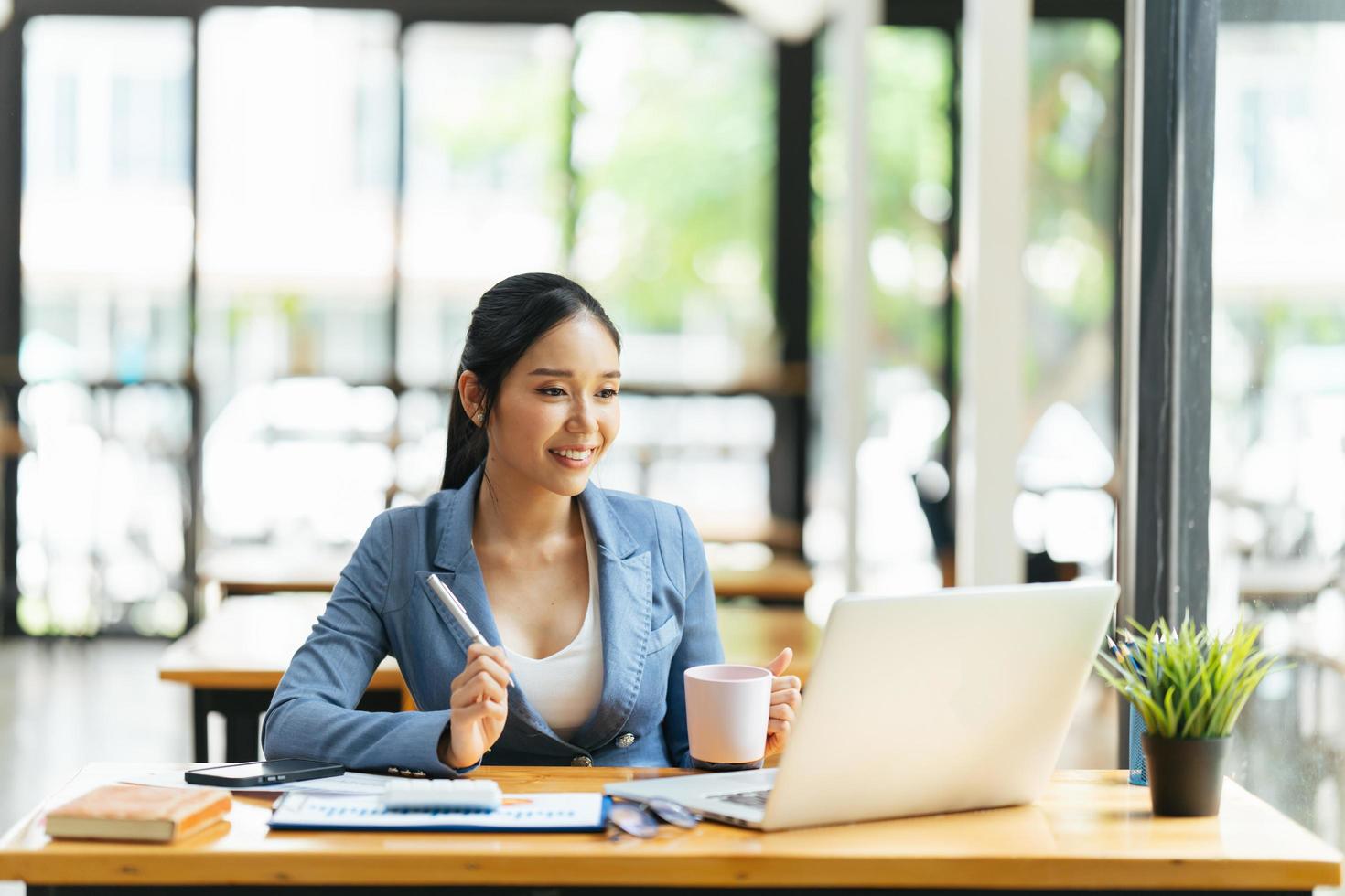 hermosa joven mujer de negocios asiática tomando café y usando una computadora portátil mientras trabaja en la oficina. foto