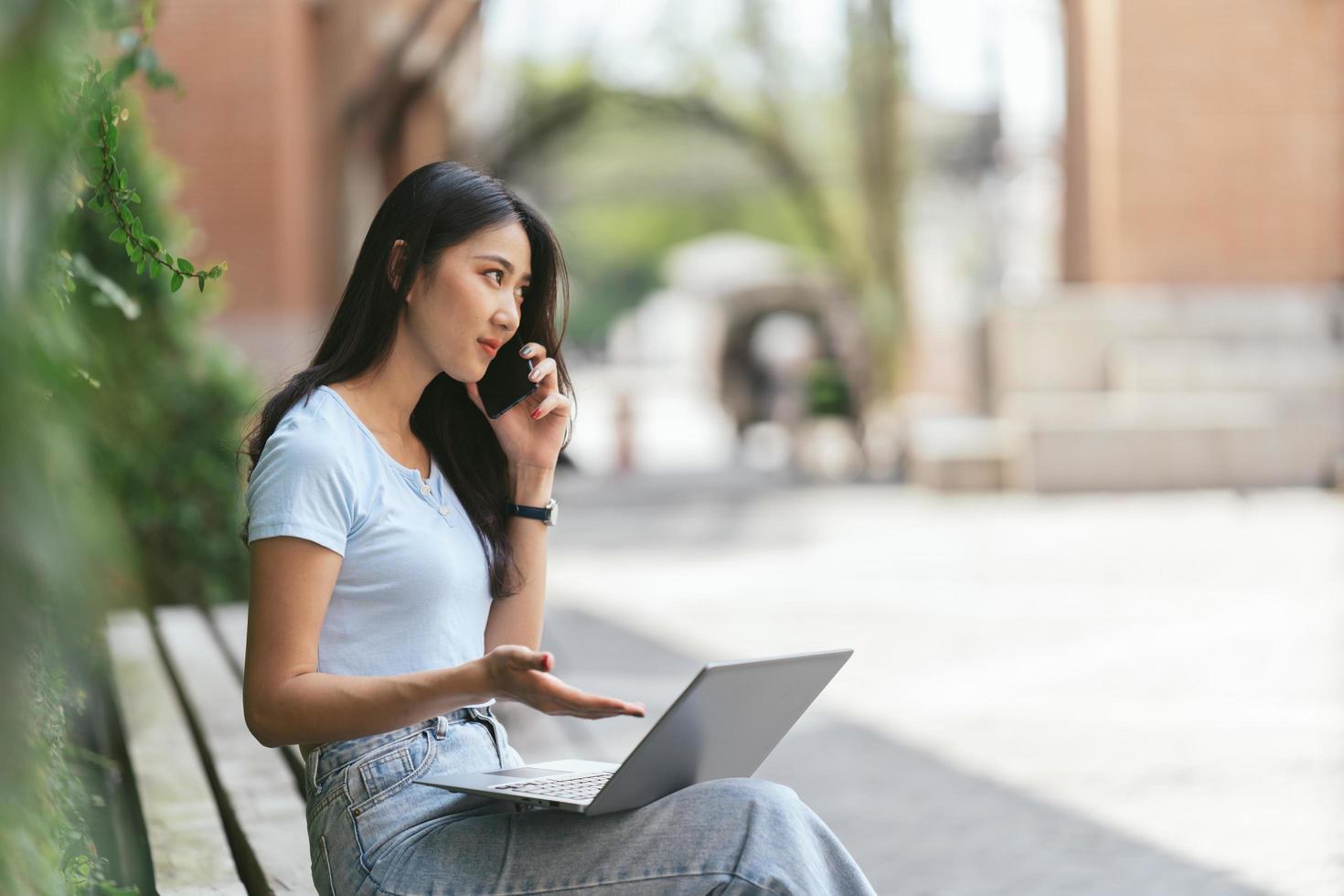 retrato de una hermosa mujer asiática sentada al aire libre durante el verano, usando una computadora portátil y un teléfono inteligente con tecnología inalámbrica inteligente, relajándose en un café restaurante. foto