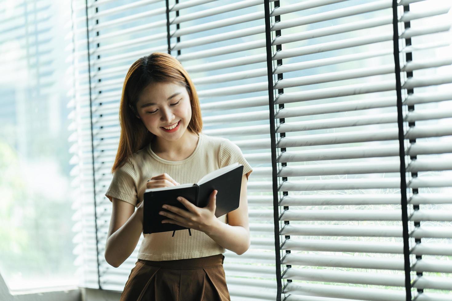 una joven mujer de negocios asiática está parada en un escritorio y tomando notas en un cuaderno. el concepto de educación y tecnología. foto