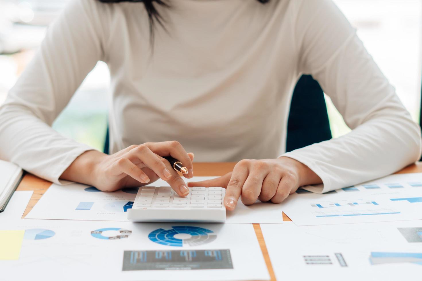 Close up hand of businessman or accountant hand holding pen working on calculator to calculate business data, accountancy document and laptop computer at office, business concept. photo