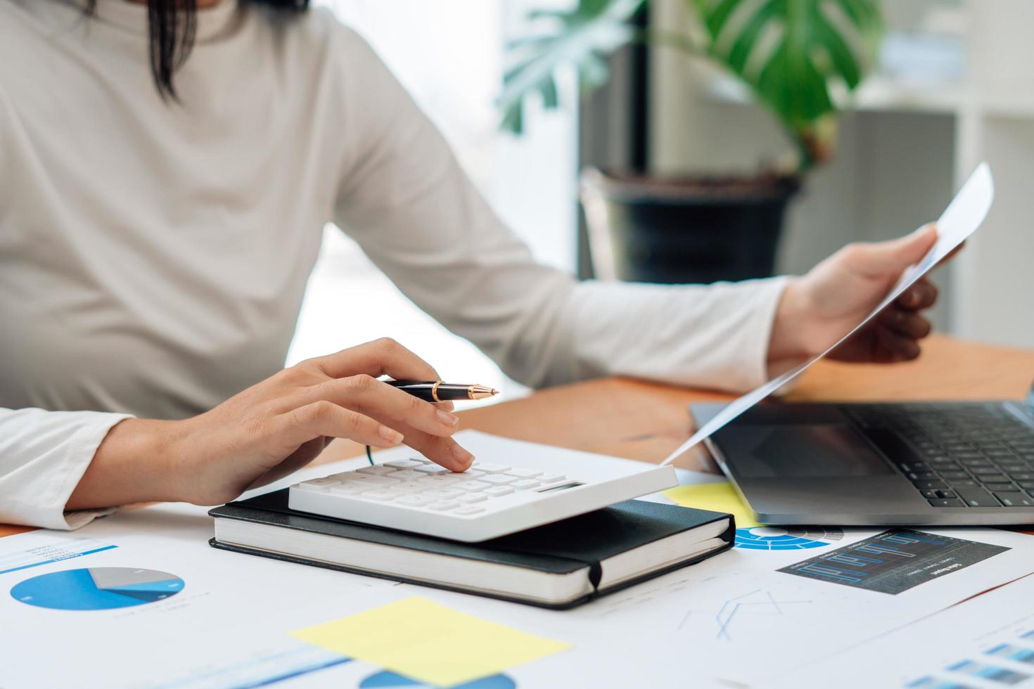 cerca de la mano del empresario o contador mano sosteniendo la pluma trabajando en la calculadora para calcular datos comerciales, documentos contables y computadora portátil en la oficina, concepto de negocio. foto