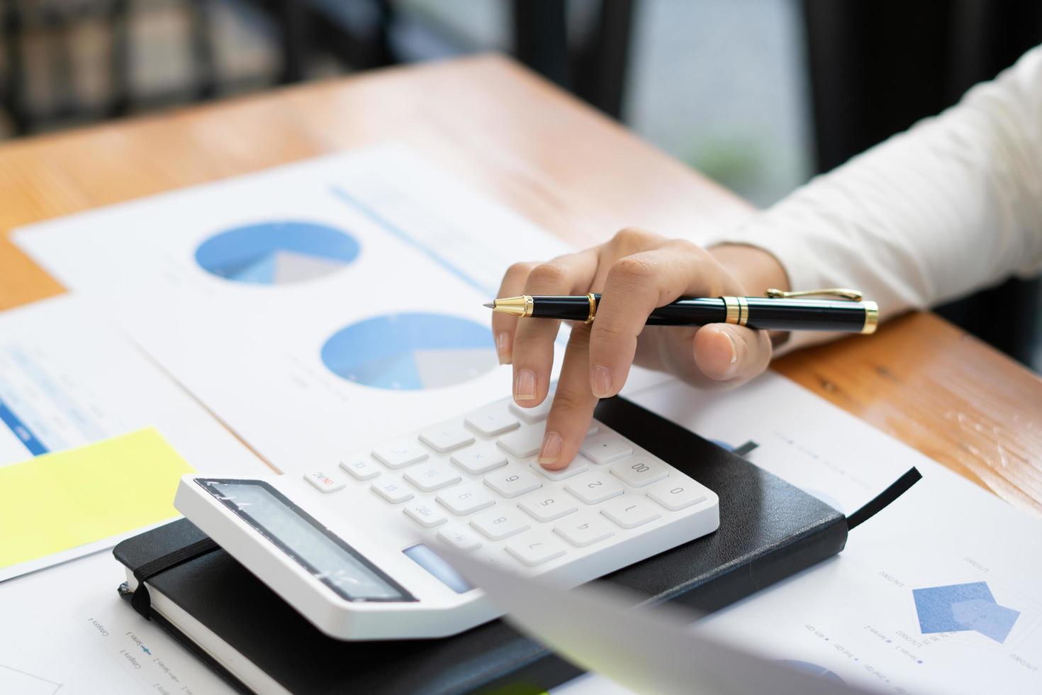 Close up hand of businessman or accountant hand holding pen working on calculator to calculate business data, accountancy document and laptop computer at office, business concept. photo