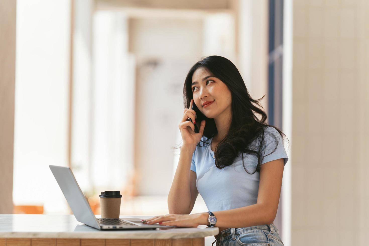 Asian woman in casual clothes is happy and cheerful while communicating with her smartphone and working in a coffee shop. photo