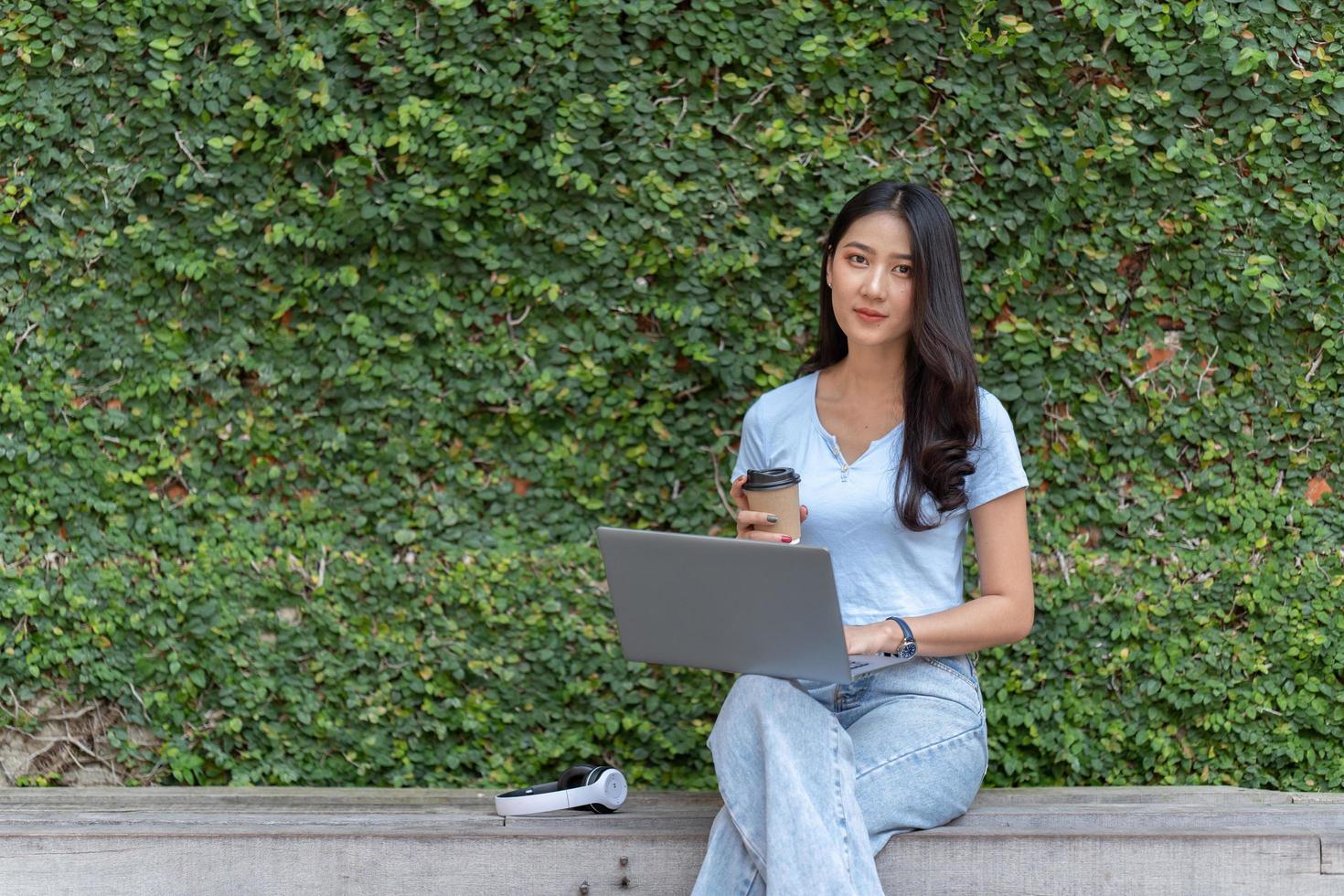 Portrait of beautiful Asian woman sitting outdoors at coffee shop restaurant during summer, using smart wireless technology computer laptop and smartphone, relaxing coffee break at cafe restaurant. photo