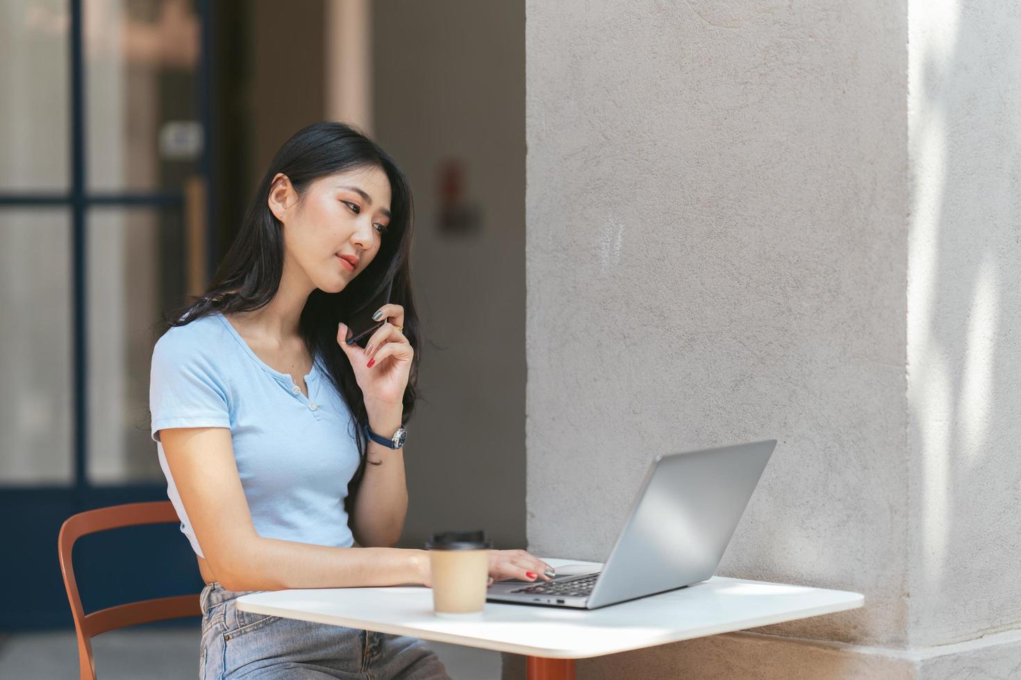 Portrait of beautiful Asian woman sitting outdoors at coffee shop restaurant during summer, using smart wireless technology computer laptop and smartphone, relaxing coffee break at cafe restaurant. photo