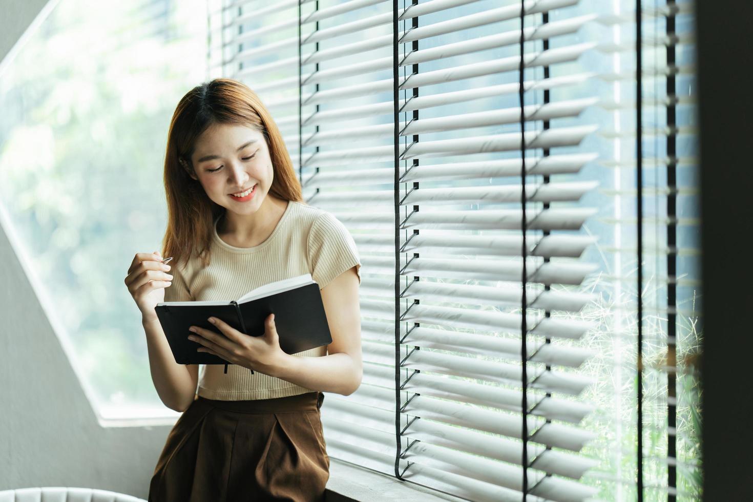 una joven mujer de negocios asiática está parada en un escritorio y tomando notas en un cuaderno. el concepto de educación y tecnología. foto