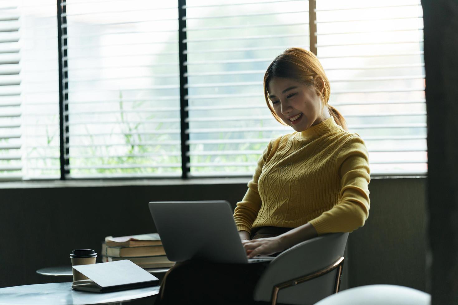 Portrait of beautiful Asian woman sitting indoors at coffee shop restaurant during summer, using smart wireless technology computer laptop and smartphone, relaxing coffee break at cafe restaurant. photo