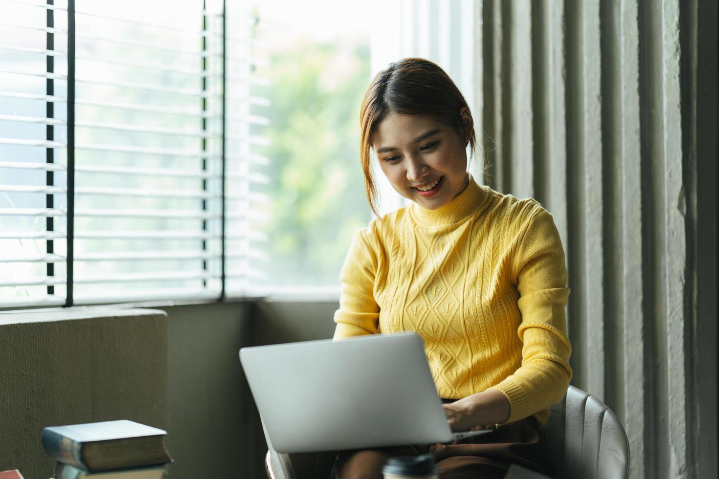 retrato de una hermosa mujer asiática sentada en el interior de un restaurante cafetería durante el verano, usando una computadora portátil y un teléfono inteligente con tecnología inalámbrica inteligente, relajándose en un café restaurante. foto