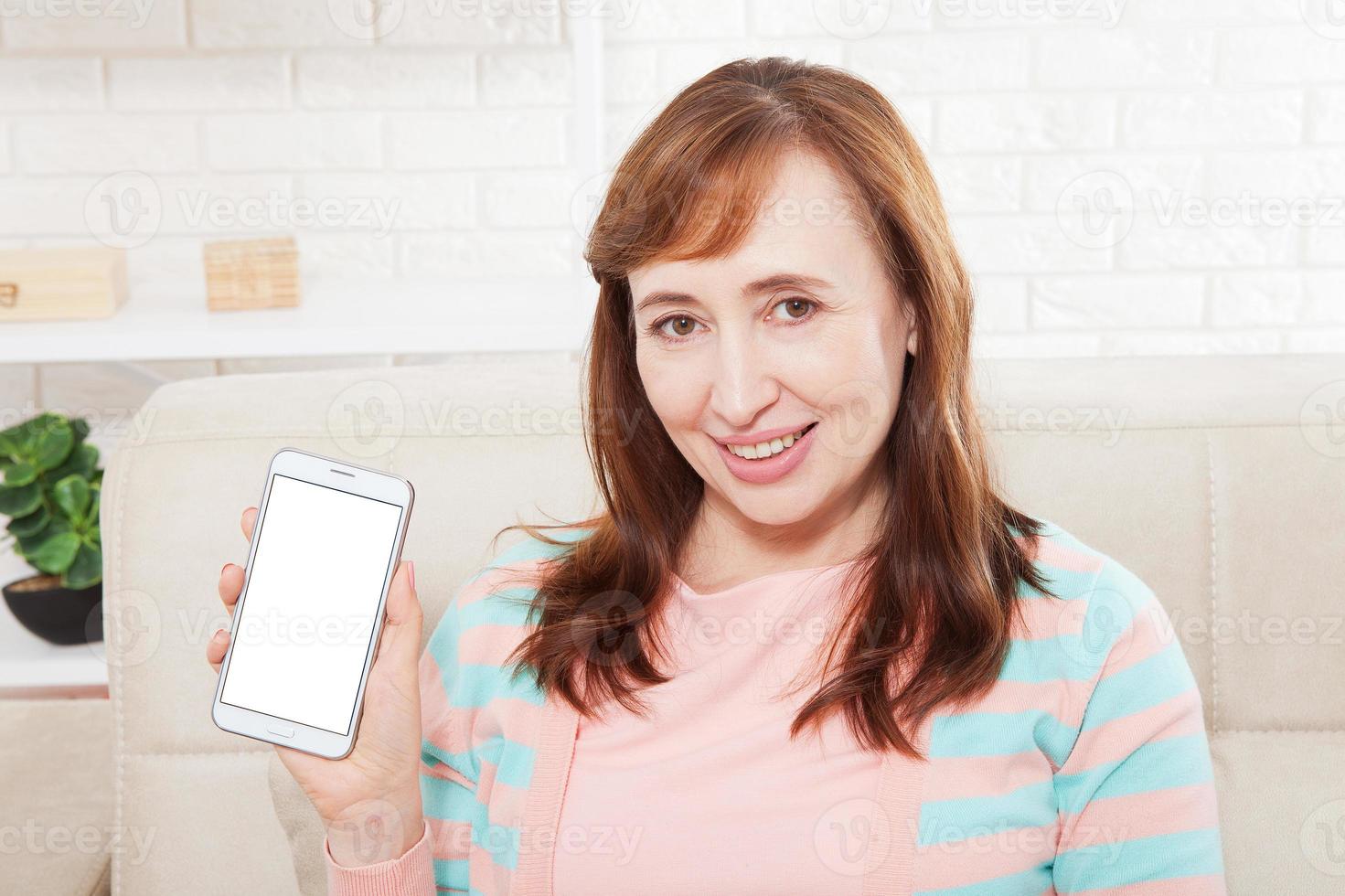 Female hand holding white phone on white clipping path inside at home background. Middle age woman. Copy space and mock up photo