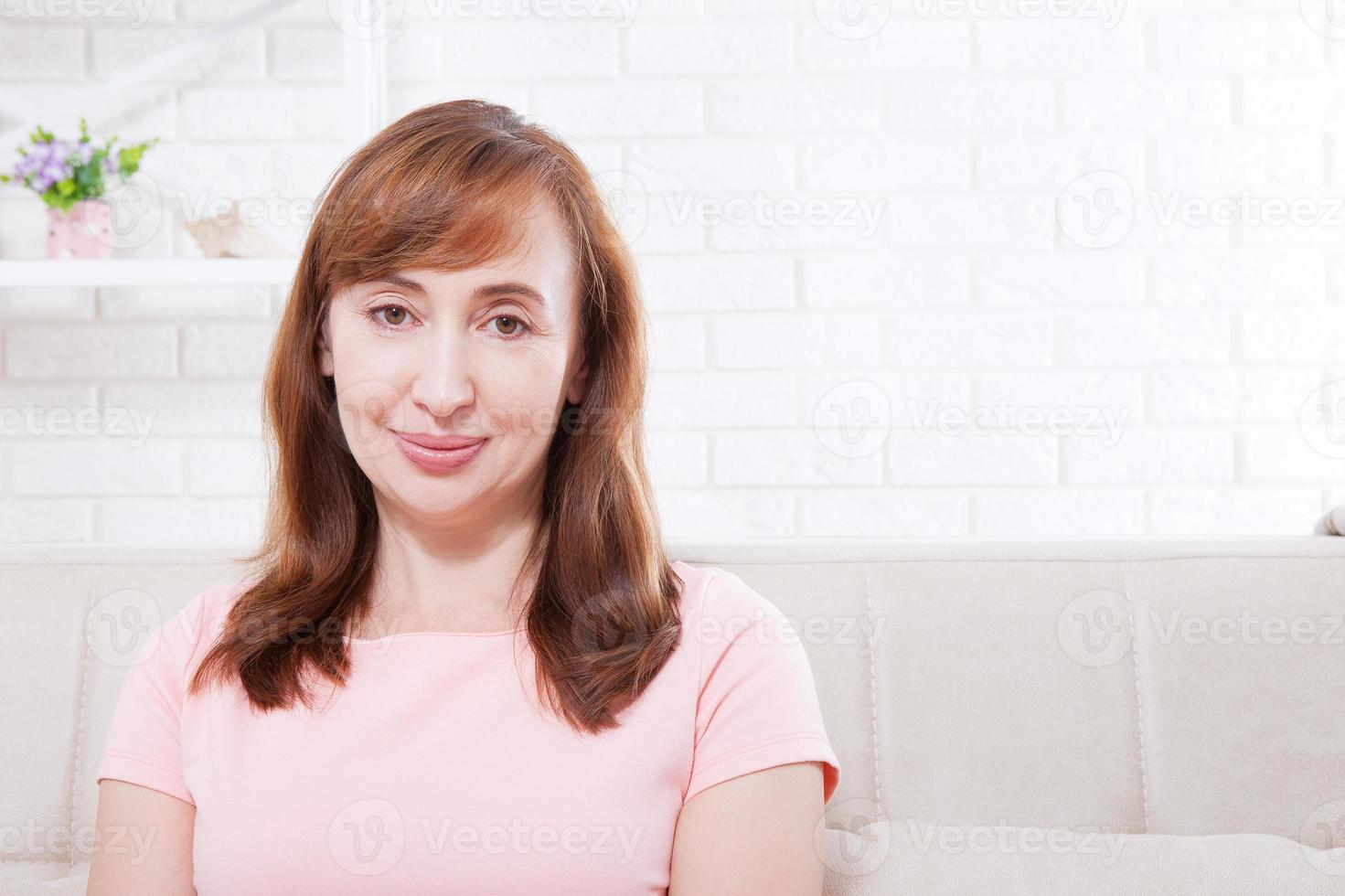 Macro portrait of smiling female face. Attractive and beautiful middle aged woman sitting on sofa and relaxing at home. Menopause photo