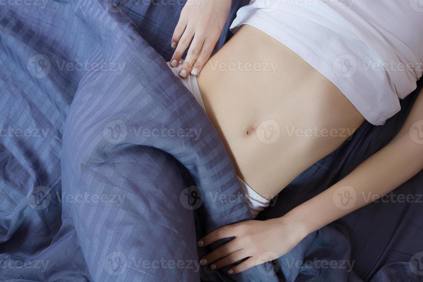 Healthy nutrition and belly health concept. Close up of woman flat stomach. Girl in bed with hungry feeling. Top view photo