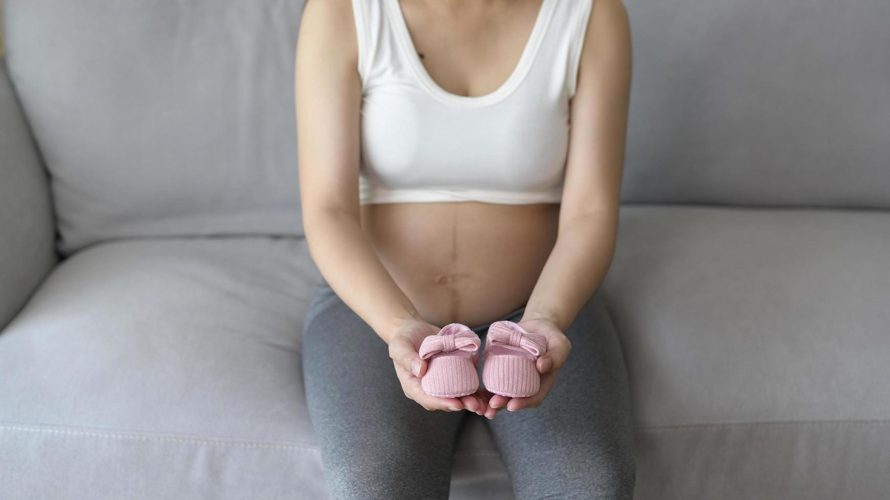 Young pregnant woman putting baby shoes on tummy, family and pregnancy care concept photo