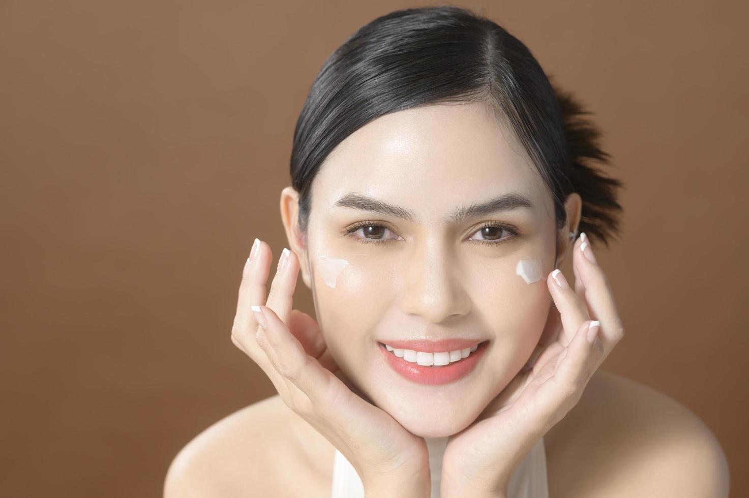 una mujer joven con una cara hermosa está sosteniendo crema, usando crema de su cara, concepto de belleza para el cuidado de la piel foto