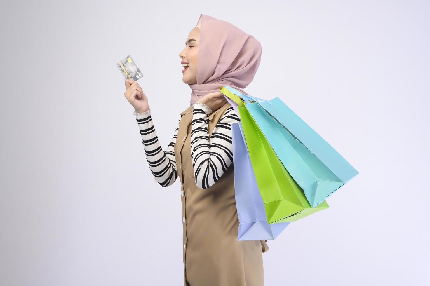 Young beautiful muslim woman in suit holding colorful shopping bags over white background studio photo