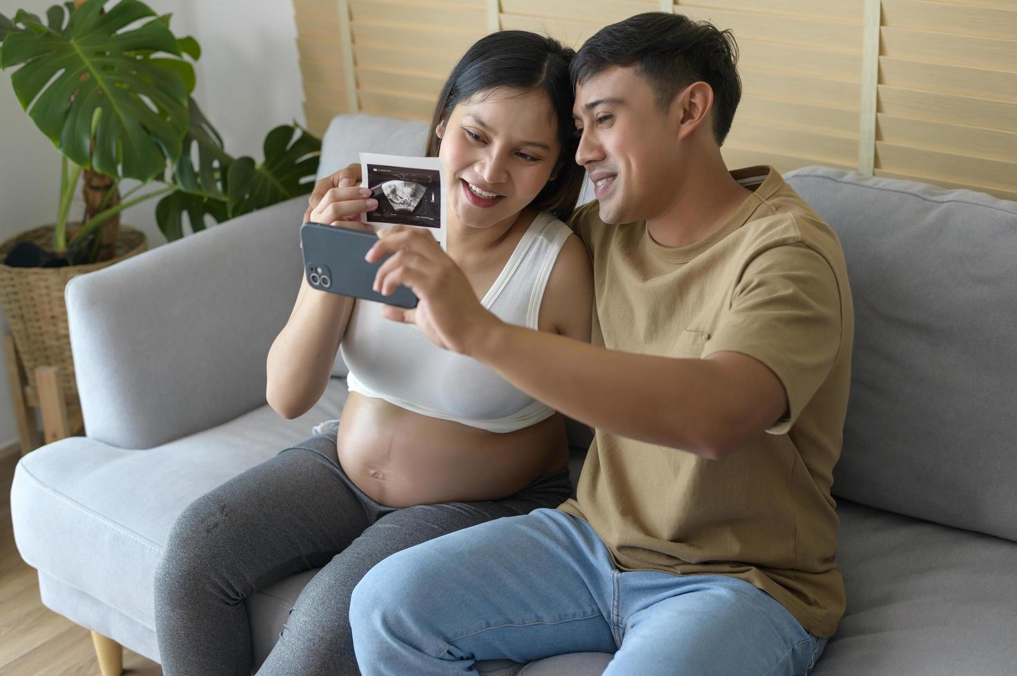 Young pregnant woman with husband embracing and video call with family and friends by smartphone on social media, family and pregnancy care concept photo