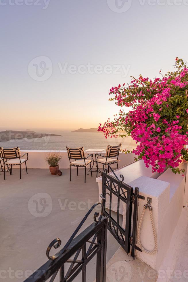 Beautiful view of Caldera and enjoying romantic scenery sunset Aegean sea, Santorini. Couple travel vacation, honeymoon destination. Romance with flowers, two chairs table and sea view. Luxury holiday photo