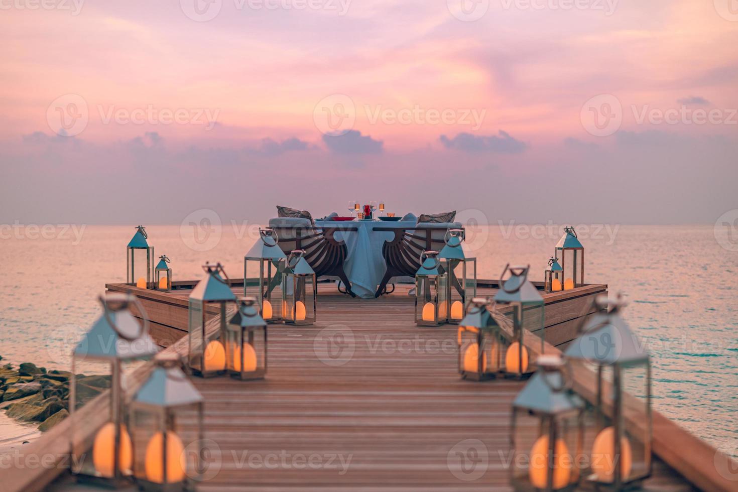 increíble cena romántica en la playa en una terraza de madera con velas bajo el cielo del atardecer. romance y amor, cenas de destino de lujo, mesa exótica con vista al mar foto