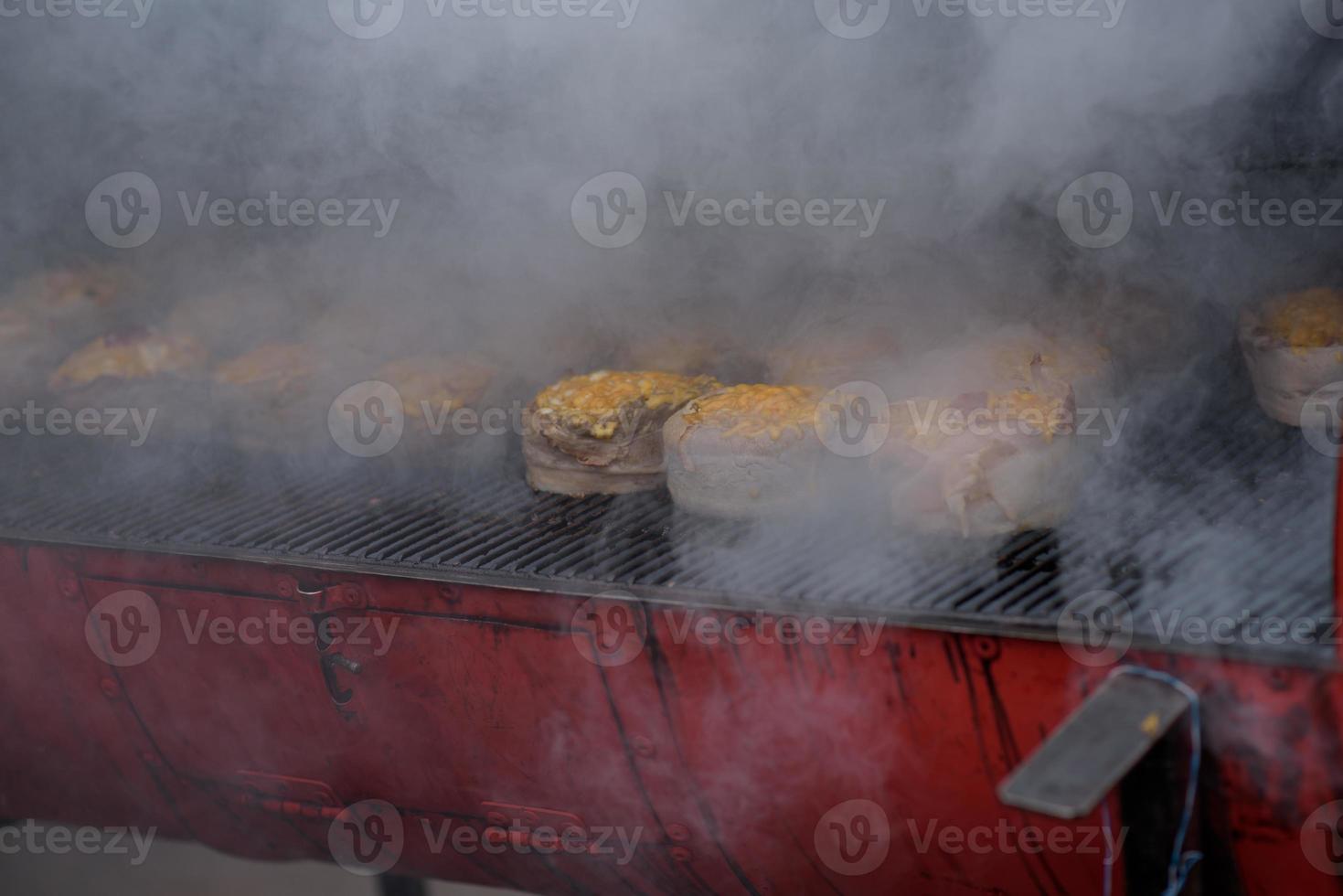 Handmade hamburger patties during the street food festival, smoke while cooking. photo