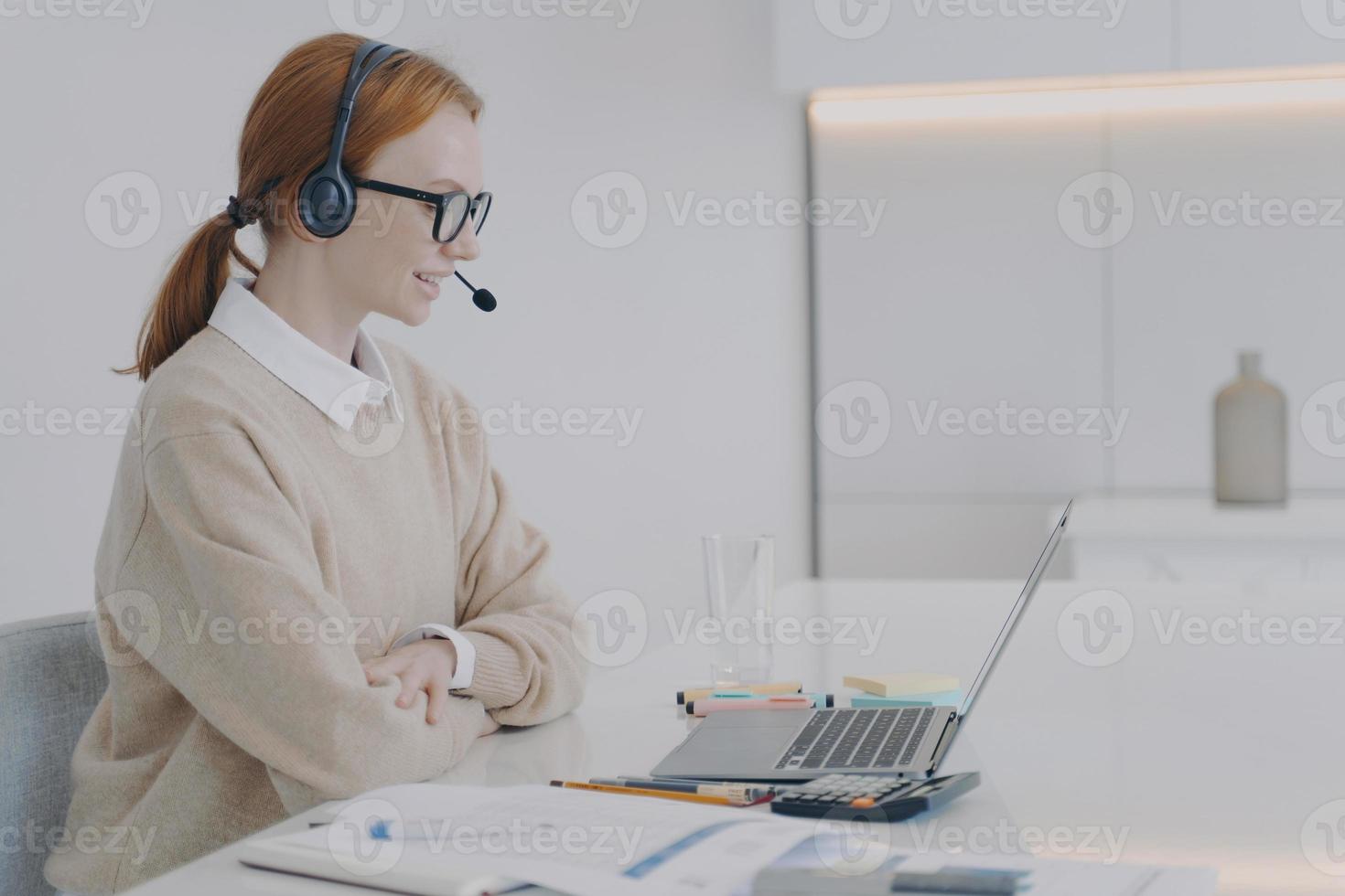 Adviser in headset is working at laptop in office. Young woman is consultant of call center. photo