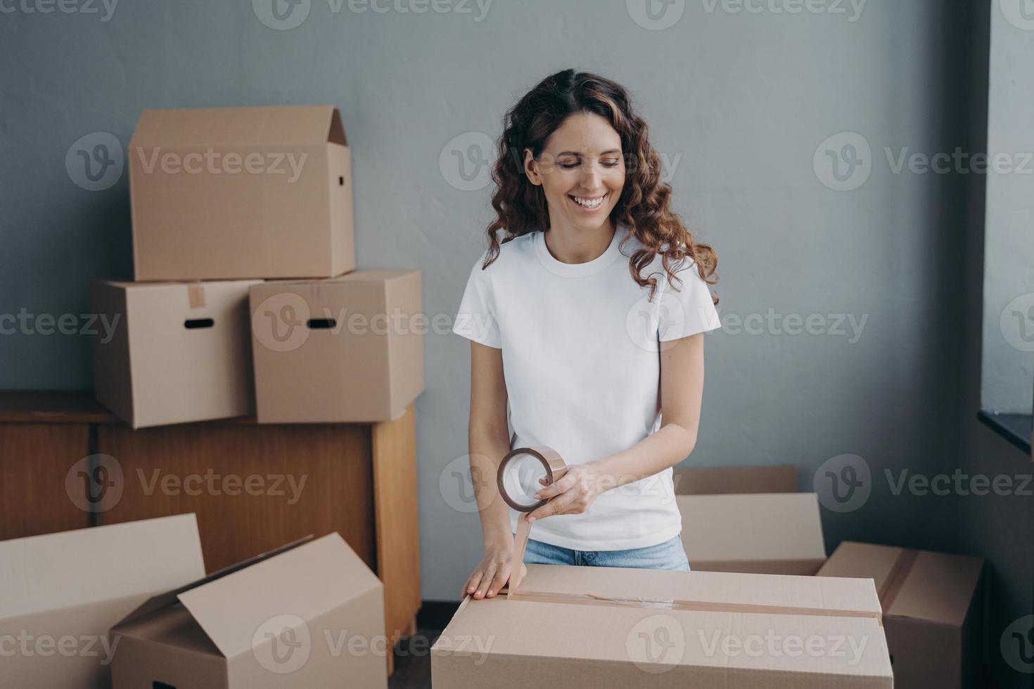 Young woman is packing cardboard containers with tape. Moving service worker preparing boxes. photo