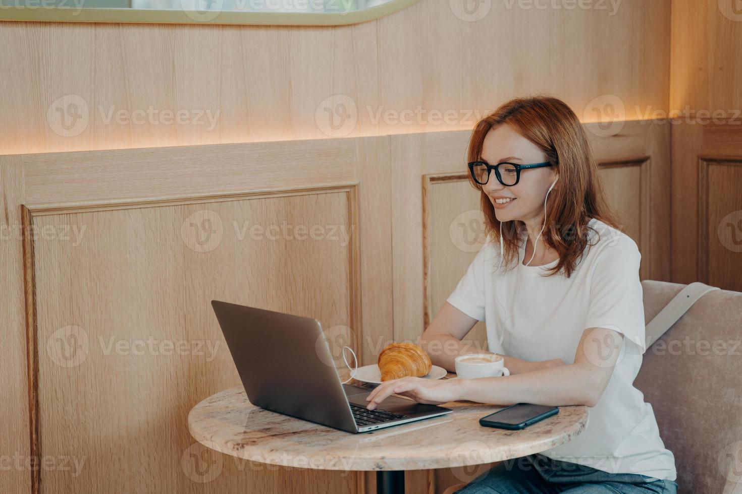 Happy smiling woman in earphones using laptop while sitting at cafe photo