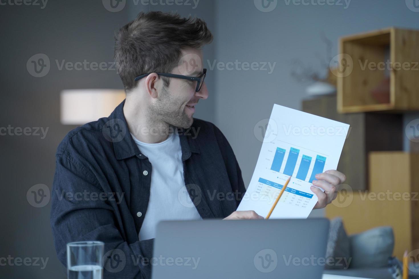 empresario alemán sonriente con gafas que representan gráficos de resultados e ingresos en una cámara portátil foto