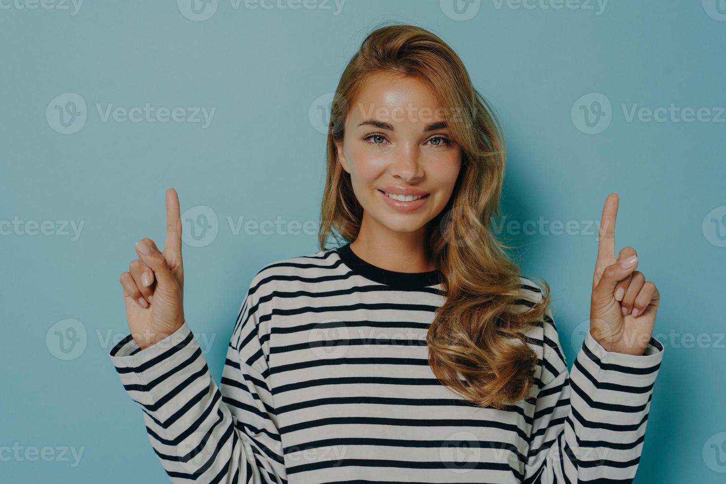 foto de una encantadora joven sonriente que señala con el dedo hacia arriba y muestra el logotipo promocional en la parte superior