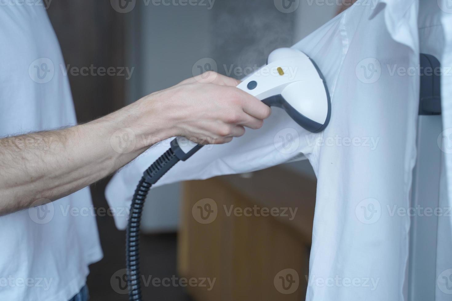 Cropped shot of man using electric garment steamer while steaming while classic shirt at home photo
