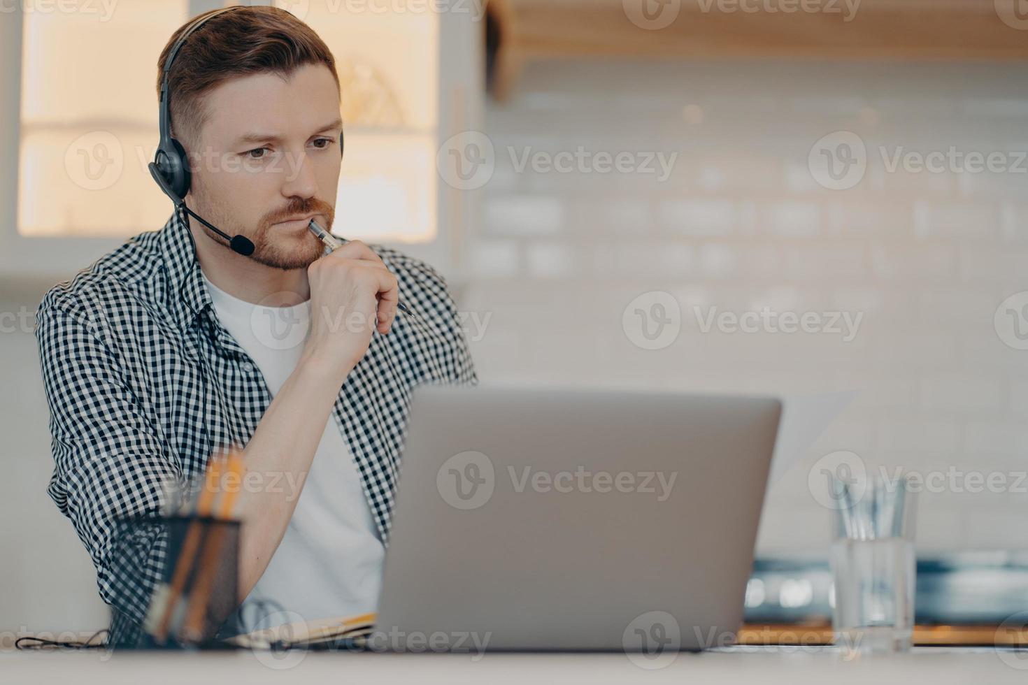 Young bearded man using headset and laptop while working at home photo