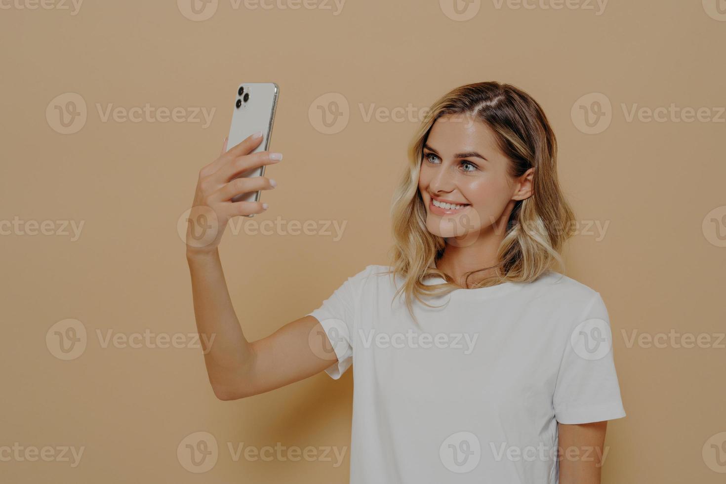 Young blonde smiling woman using smartphone while having video call with family or friend photo