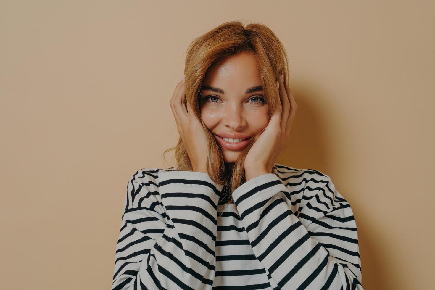 mujer joven feliz mirando a la cámara con expresión facial alegre sosteniendo su cara con ambas manos foto