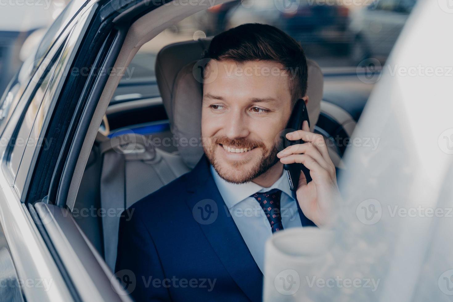 Image of young caucasian successful jurist in formal dark blue suit talking on cellphone in car photo