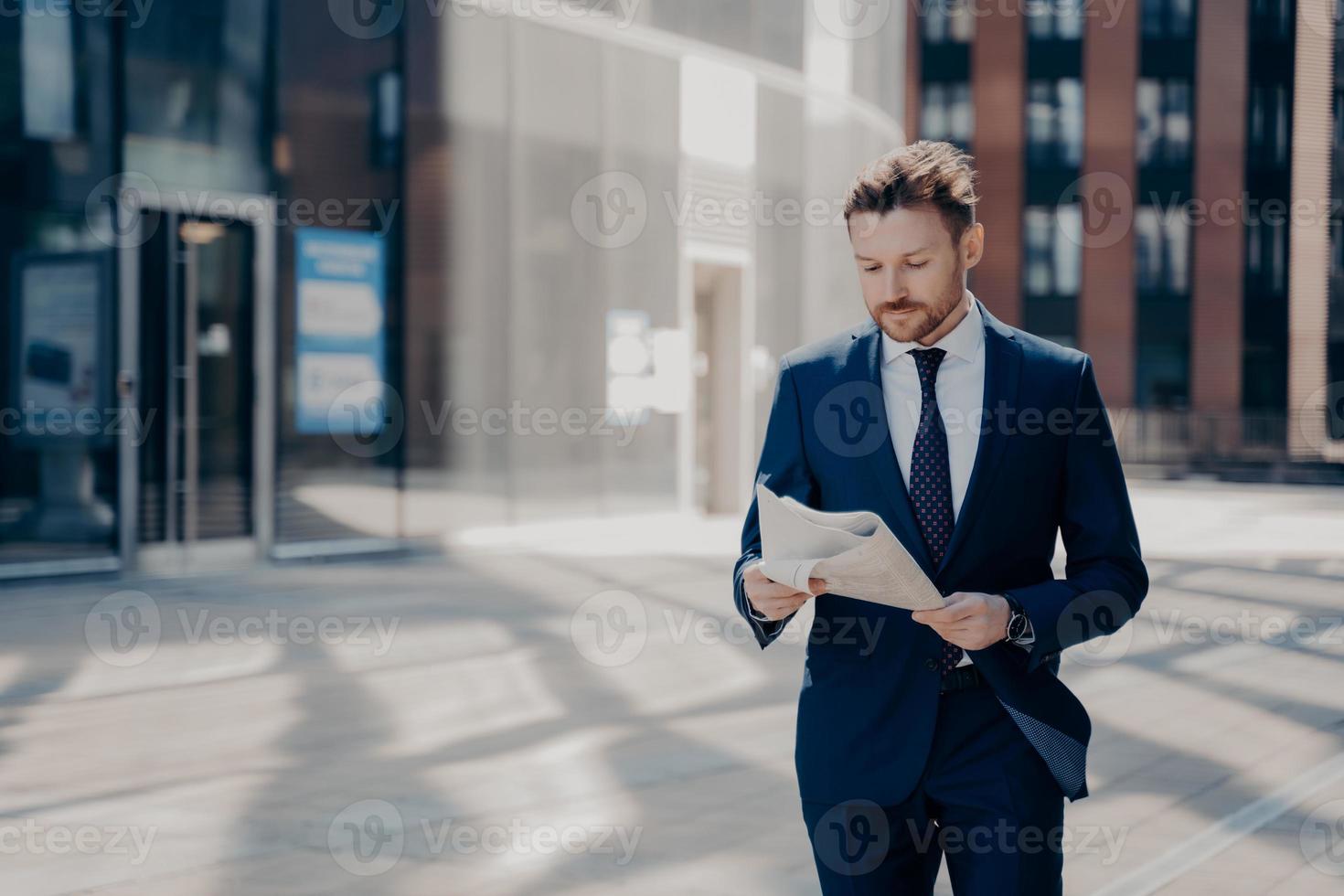 Successful businessman in formal wear reads newspaper while walking photo