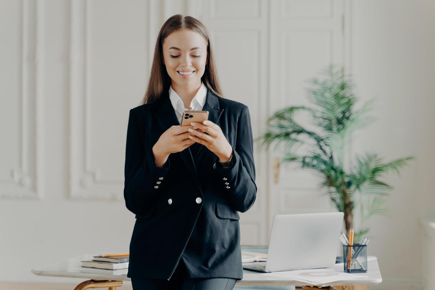 Positive young businesswoman looking at smartphone screen photo