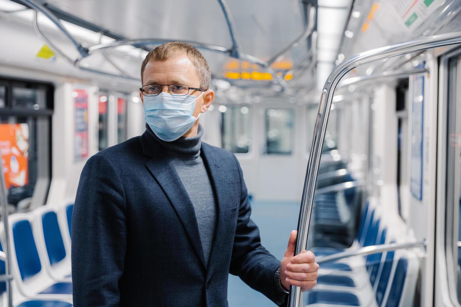 Male commuter poses in empty subway carriage, wears medical mask to prevent infected coronavirus at public metro station, looks somewhere, thinks about social distancing. Disease prevention. photo