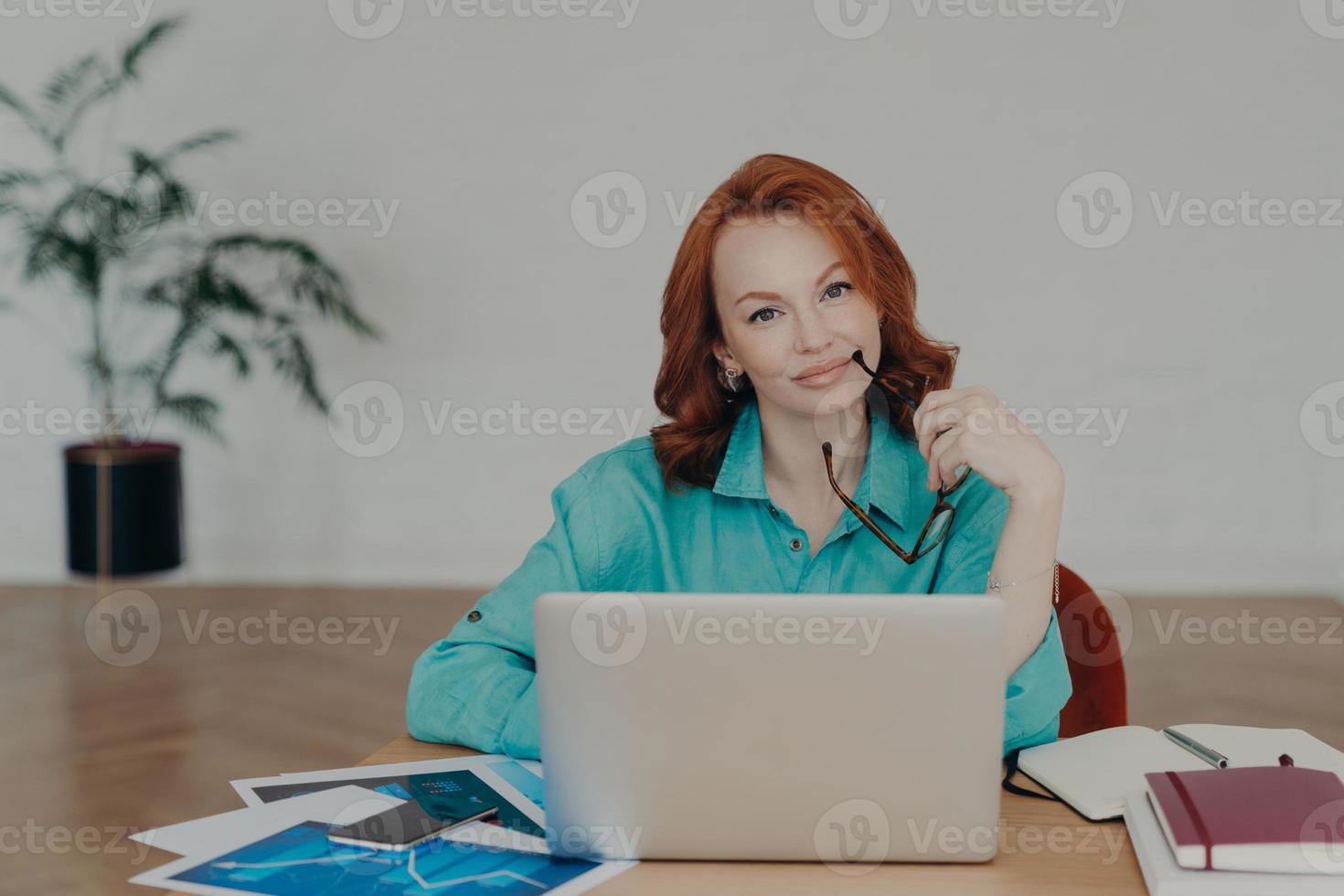 Beautiful redhead woman works distantly from home, sits in front of laptop computer finishes working on project thinks about adding interesting content on own website prepares publication for web page photo