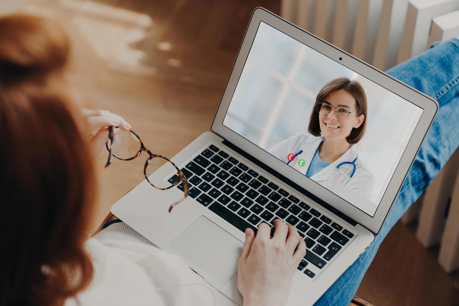 Unrecognizable woman has video chat with experienced doctor on laptop computer gets consultancy during quarantine discuss disease treatment. Videochatting with general practitioner. Back rear view photo