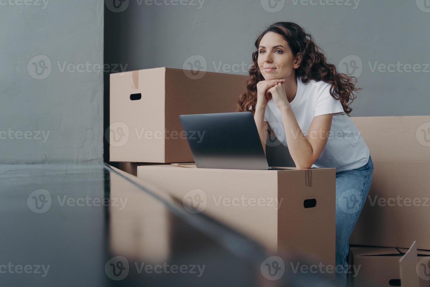 Hopeful spanish woman unpacking cardboard boxes at new place and looking through window. photo