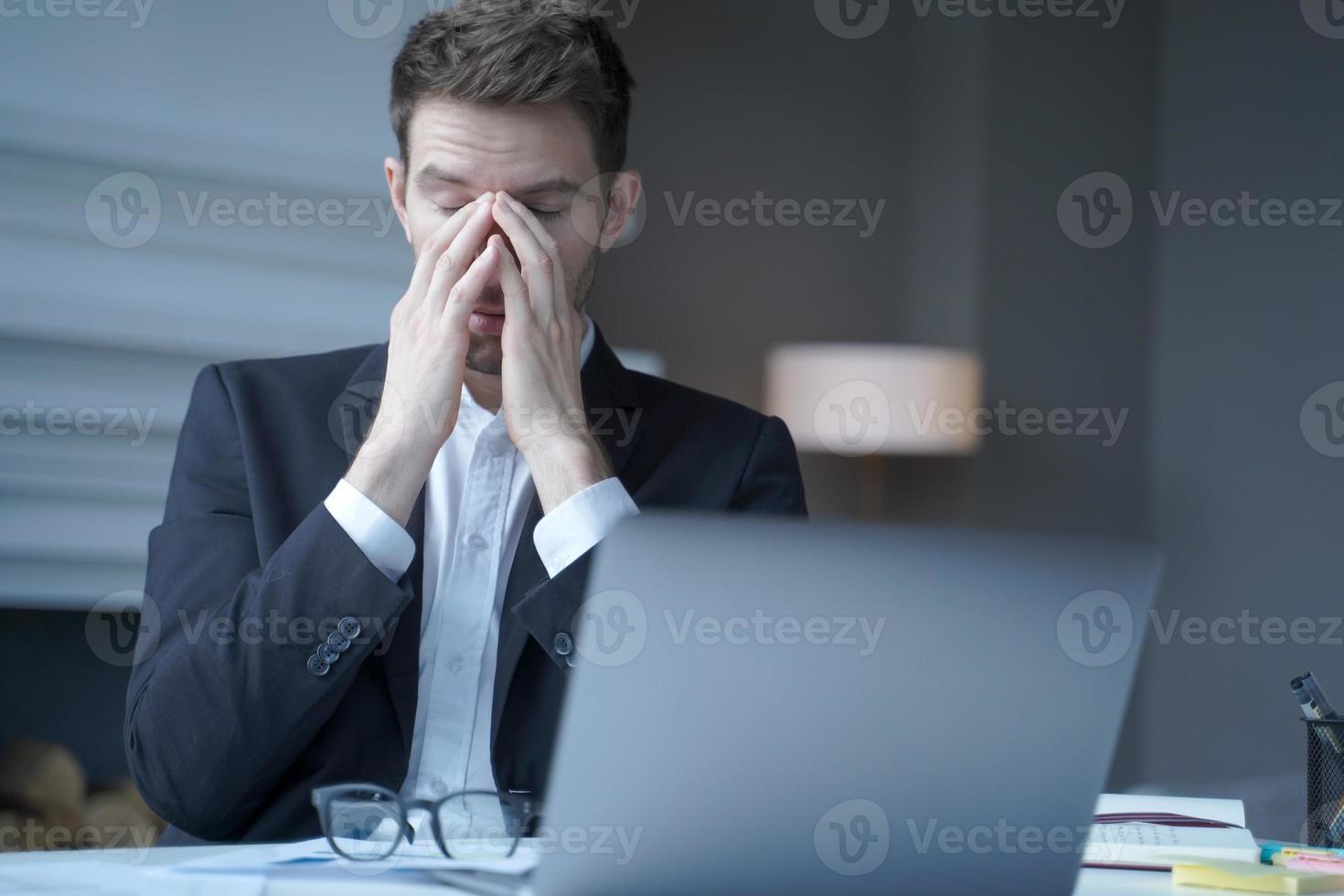 Overworked male entrepreneur sits at home office, suffering from heavy headache and fatigue photo