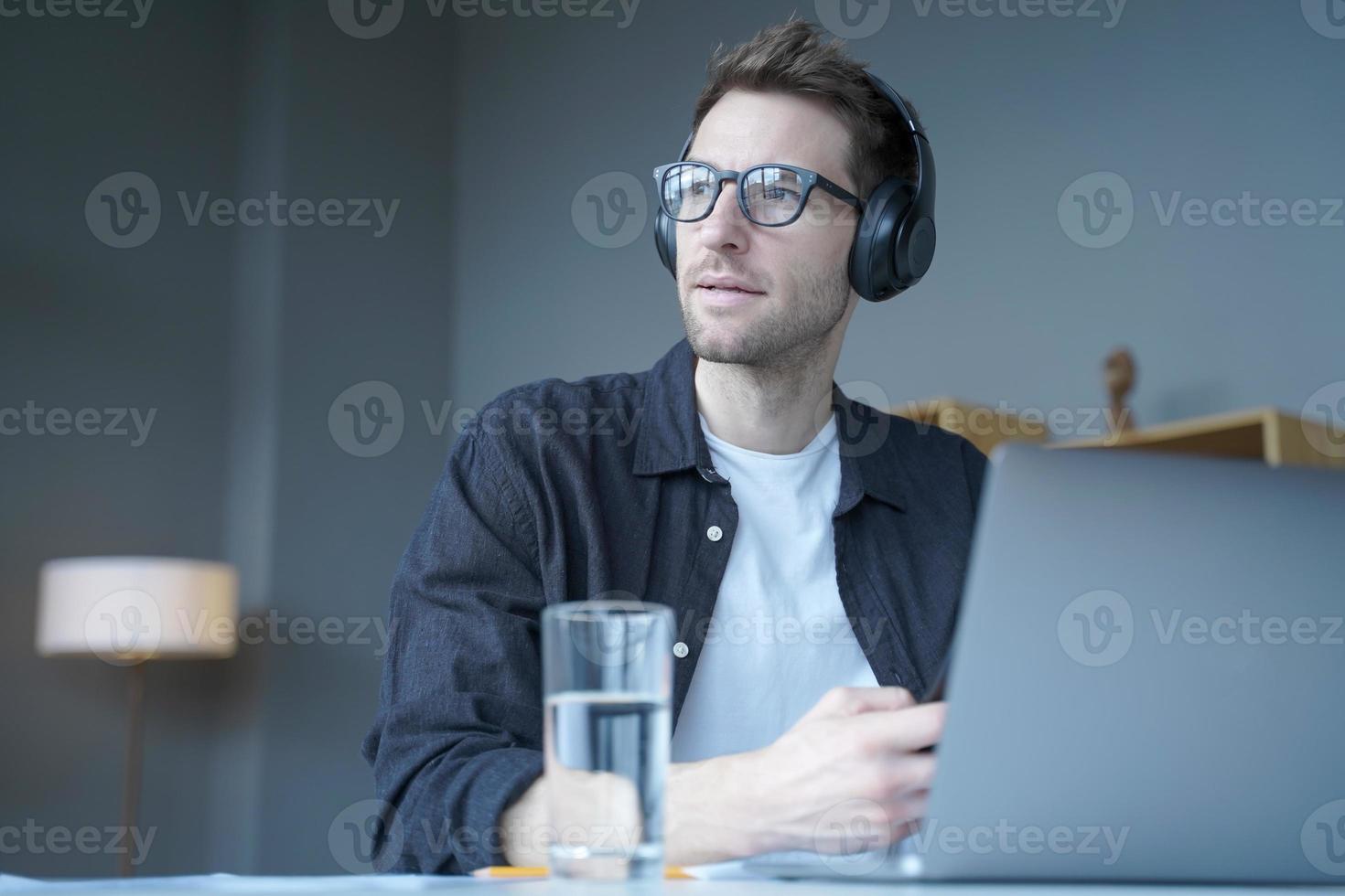 Young european man in wireless headphones listening audio podcast or watching webinar on laptop photo