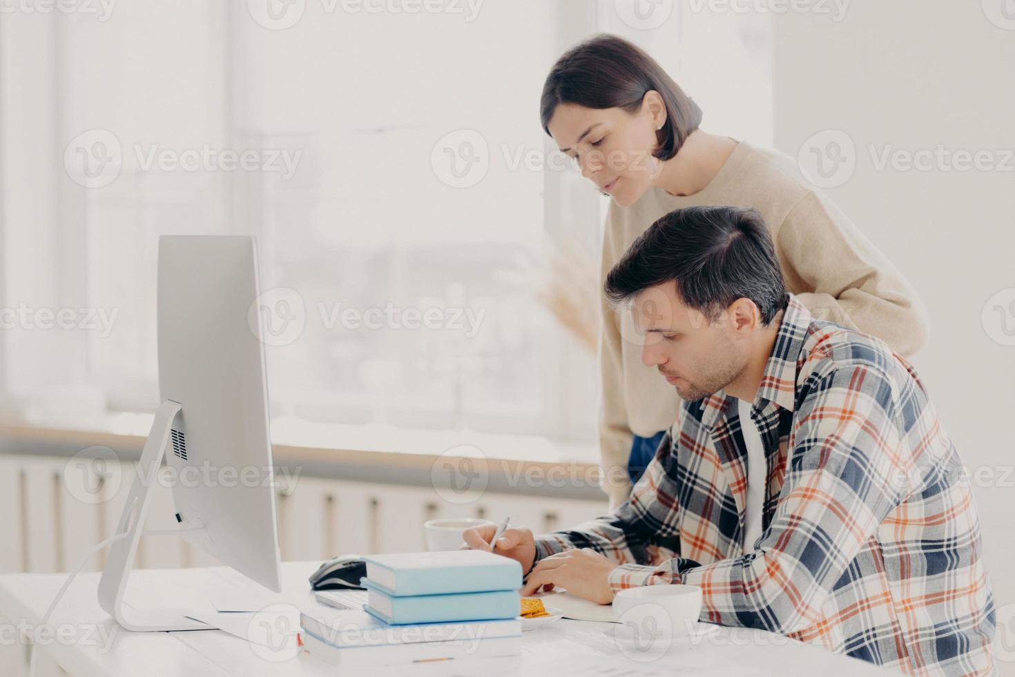 el esposo y la esposa trabajan juntos en un informe en papel, verifican la información, se sientan frente a la computadora, beben café, se visten con ropa informal, colaboran para trabajar en equipo. concepto de familia y trabajo remoto foto