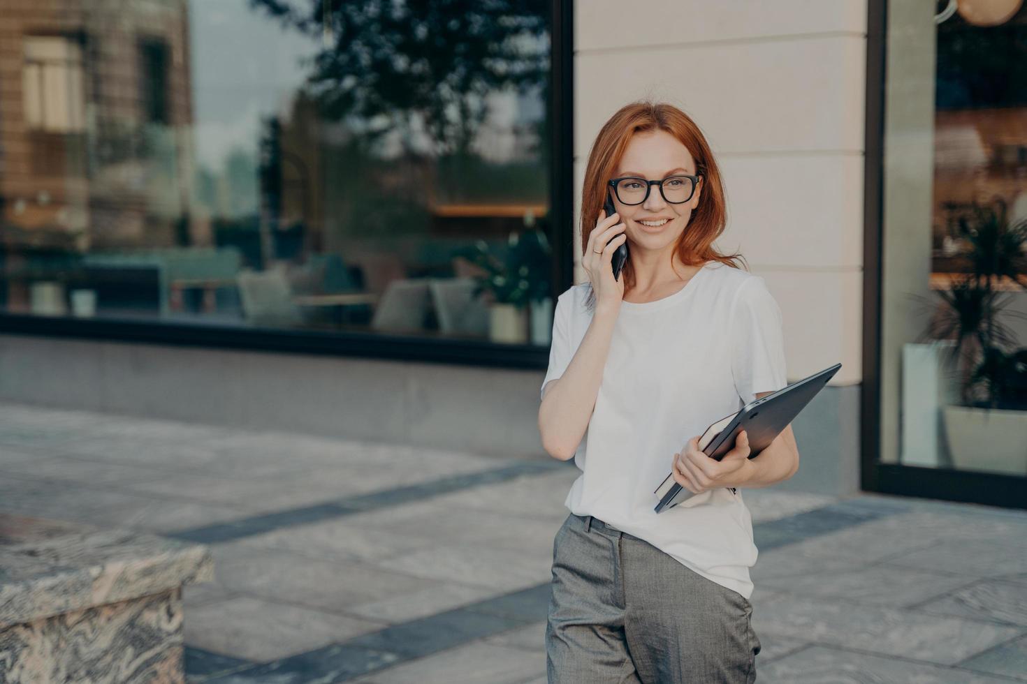 Woman has telephone conversation discusses coming meeting with friend carries tablet notebook photo